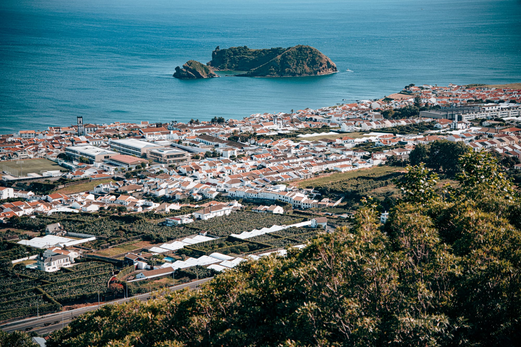 Overhead view of the red-roofed town of Vila Franca do Campo with Ilhéu de Vila Franca do Campo rising from the blue Atlantic in the background