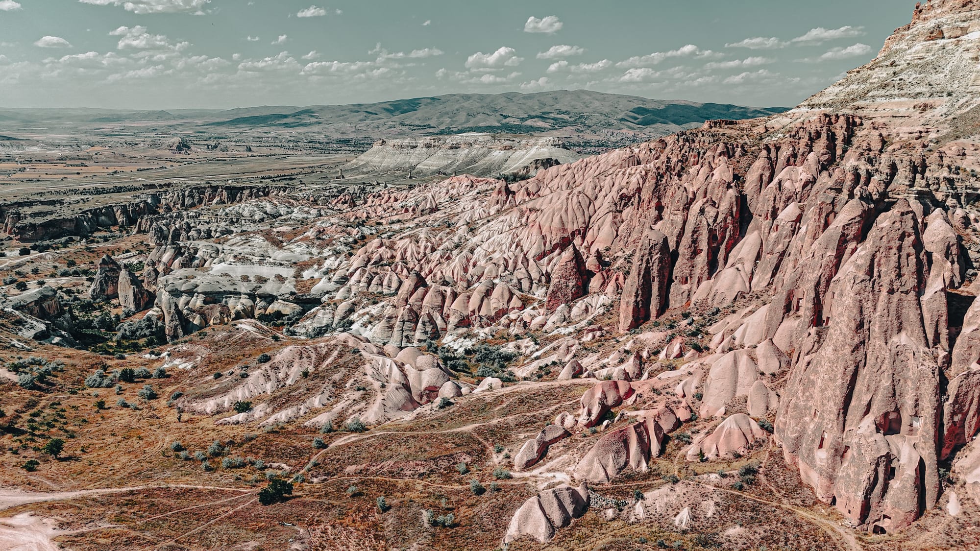 Wide view of Rose Valley in Cappadocia, Turkey, showing dramatic red and white rock formations eroded into ridges, spires, and cliffs