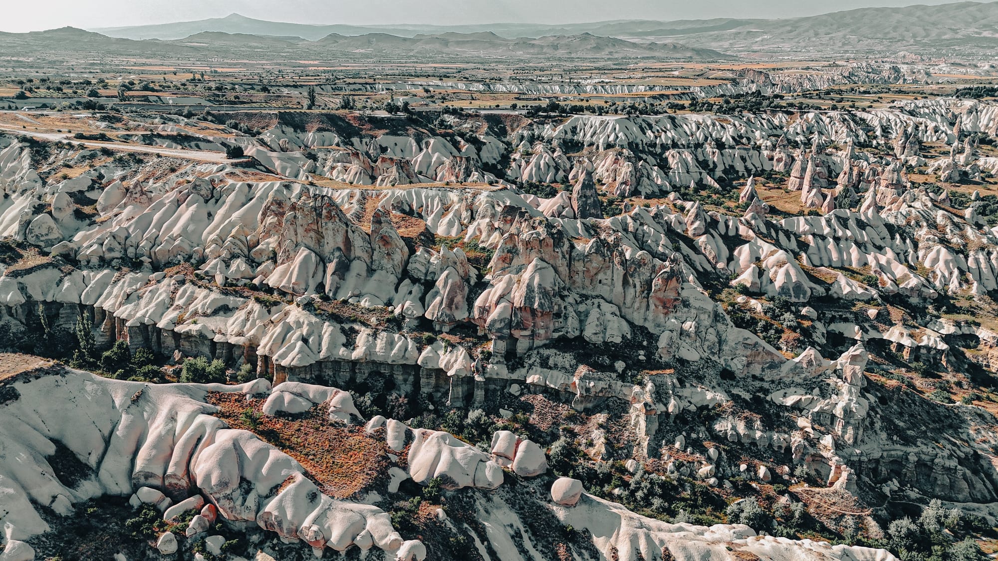 Aerial view of Cappadocia’s rugged valleys with eroded ridges, cliffs, and layered rock formations extending into the distance