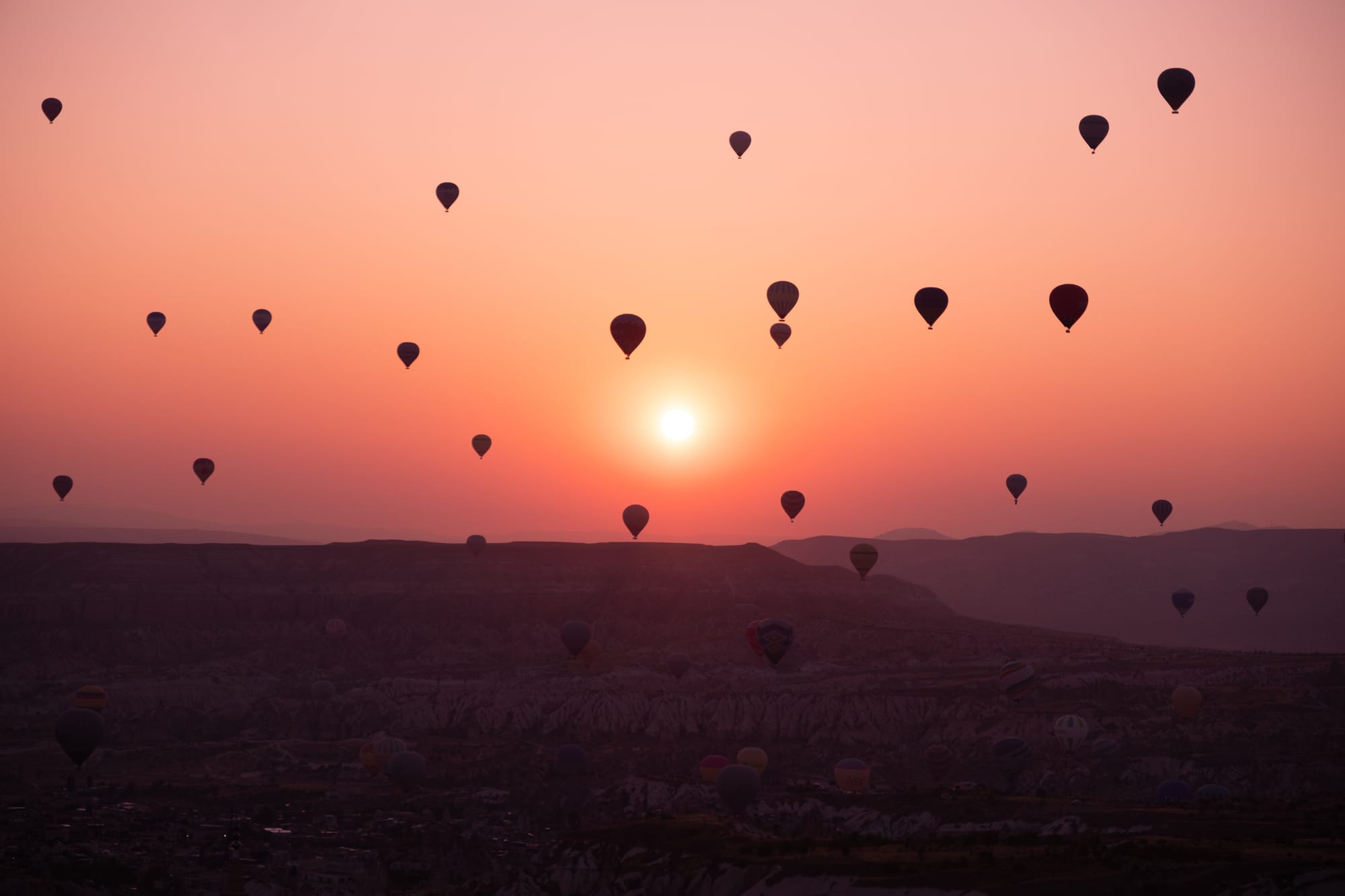 Uçhisar Cappadocia sunrise view with dozens of hot air balloons floating above valleys and ridges