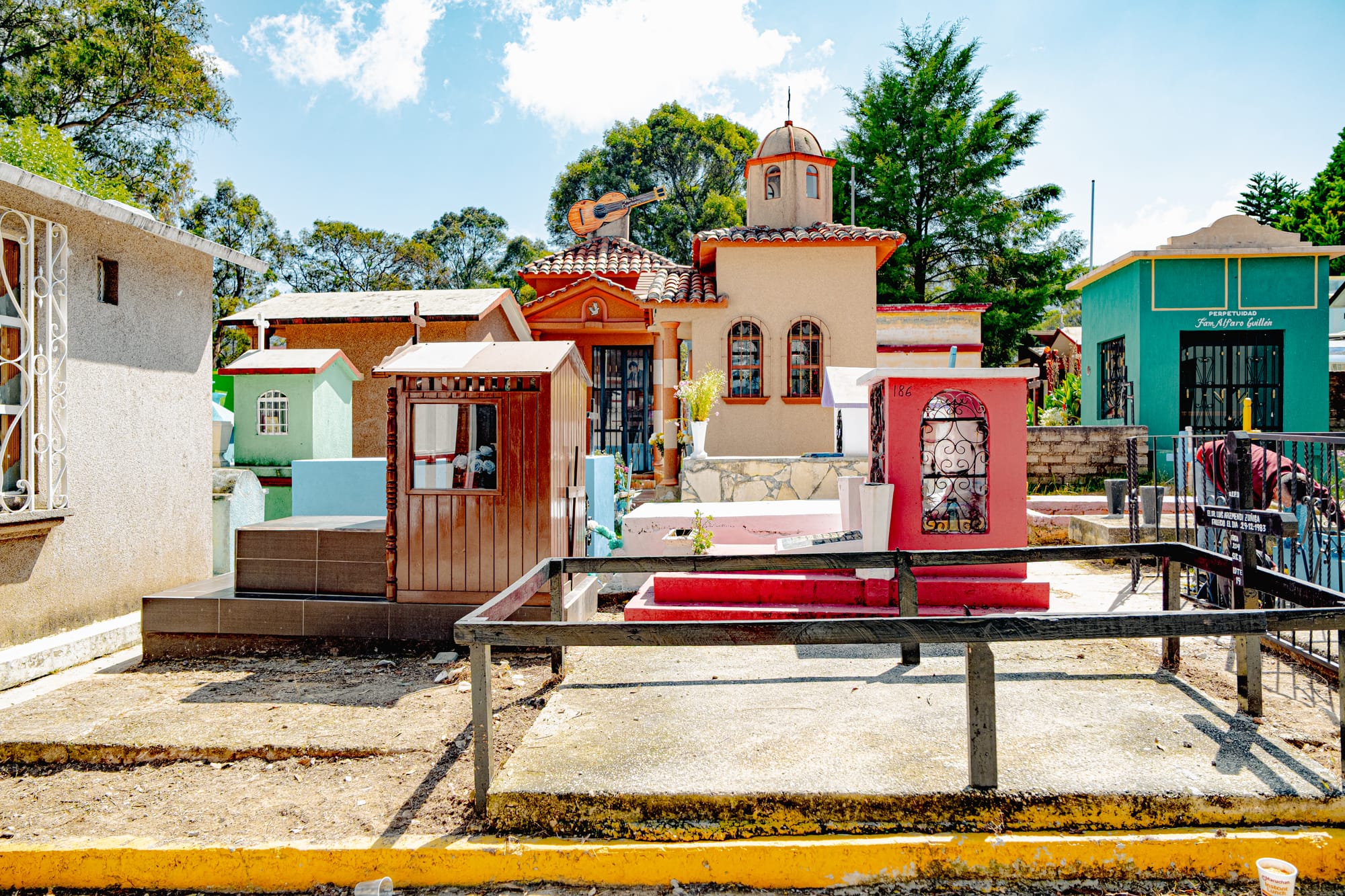 A section of the Municipal Pantheon in San Cristóbal de las Casas, showing colorful, house-like tombs with domed roofs and a guitar sculpture atop one, illustrating the blend of architecture, artistry, and devotion in Chiapas’ cemetery traditions