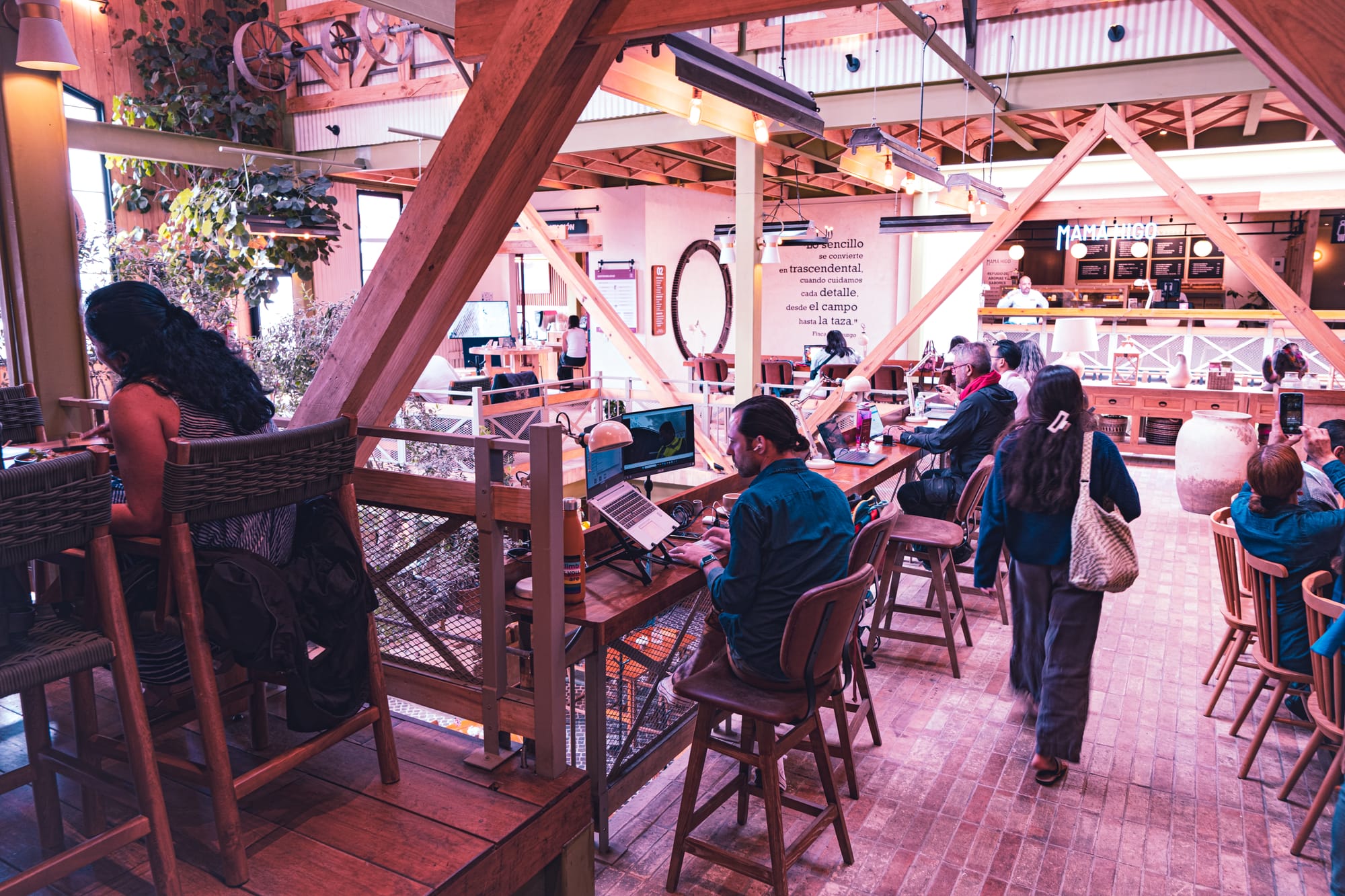 The interior of Histórico Café in San Cristóbal de las Casas, with people working at long wooden tables beneath exposed beams and the Mamá Higo bakery counter in the background