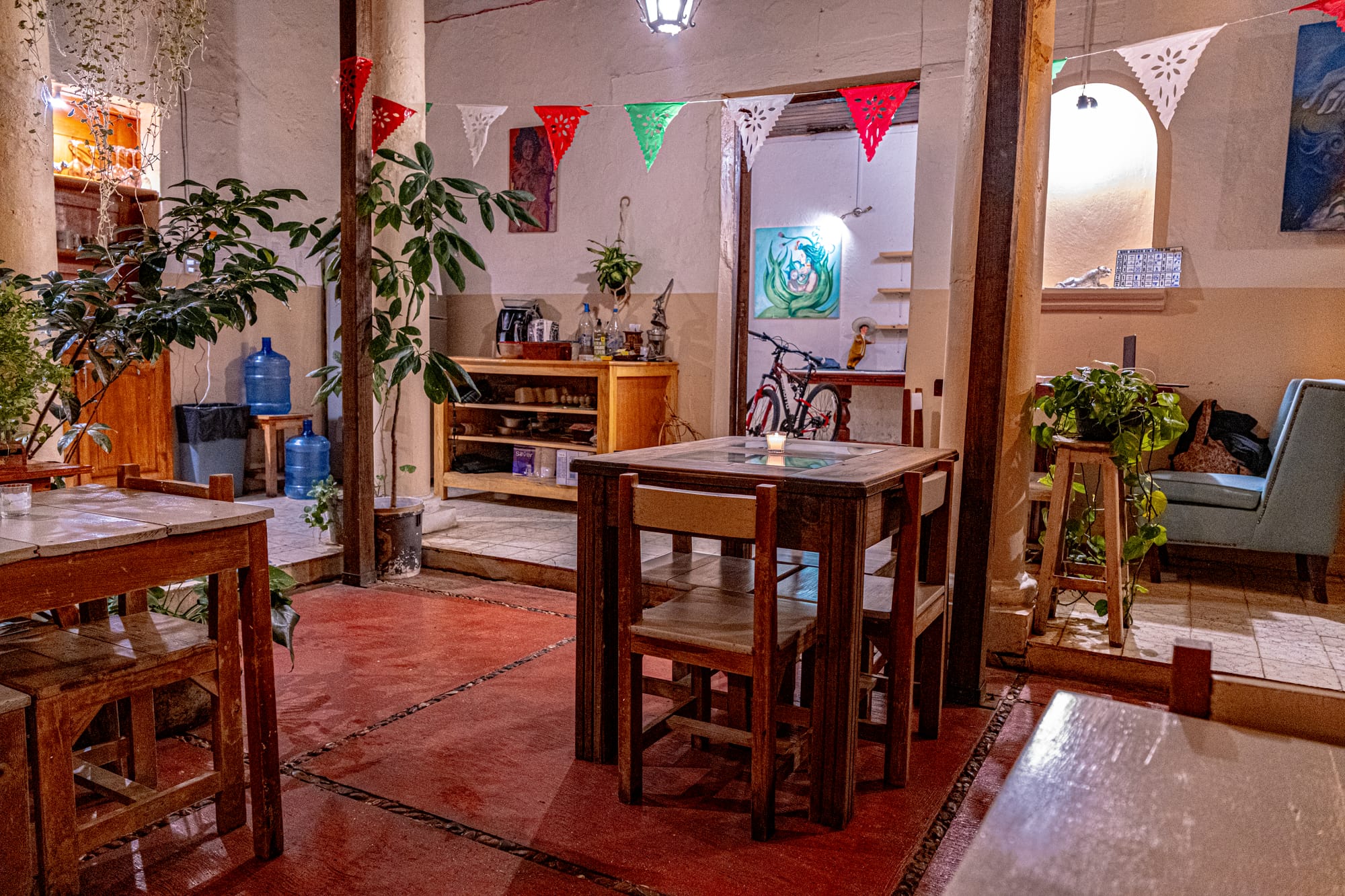 The interior of La Casa del Tamal in San Cristóbal de las Casas, featuring wooden tables, indoor plants, papel picado decorations, and a calm courtyard-style dining area