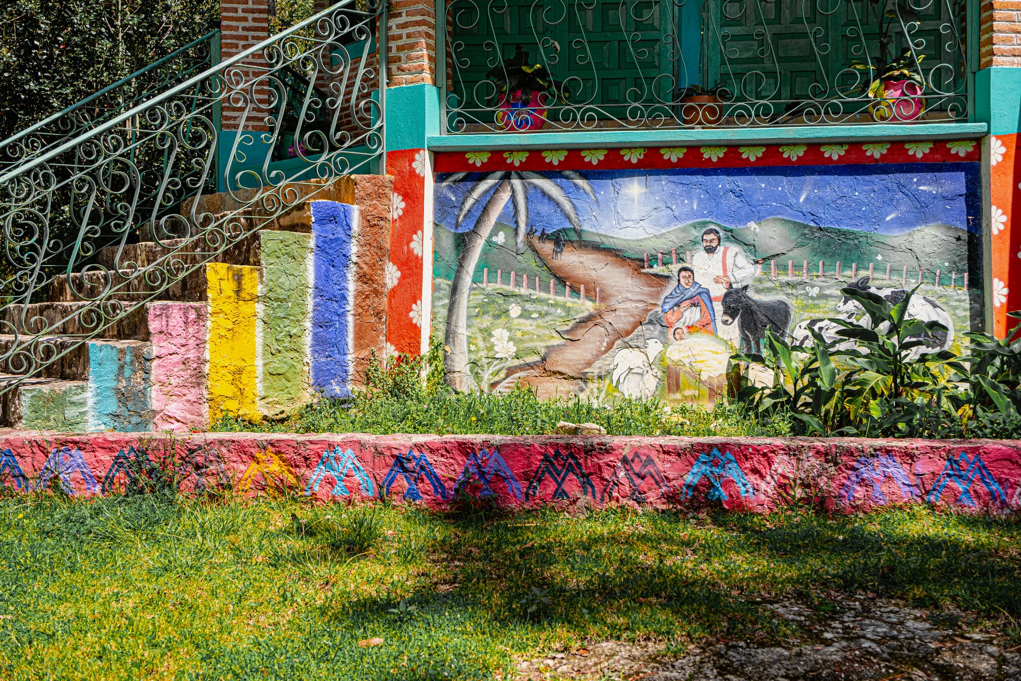 Colorful outdoor mural at CIDECI showing a pastoral scene with a family, animals, and mountains, painted beneath a staircase with multicolored steps and decorative patterns on the surrounding walls