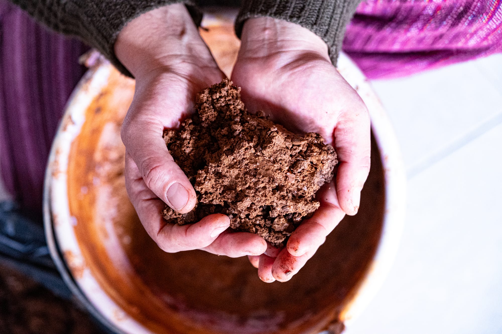 Hands holding a piece of damp, reddish clay over a large bowl inside Itzel’s mountain home