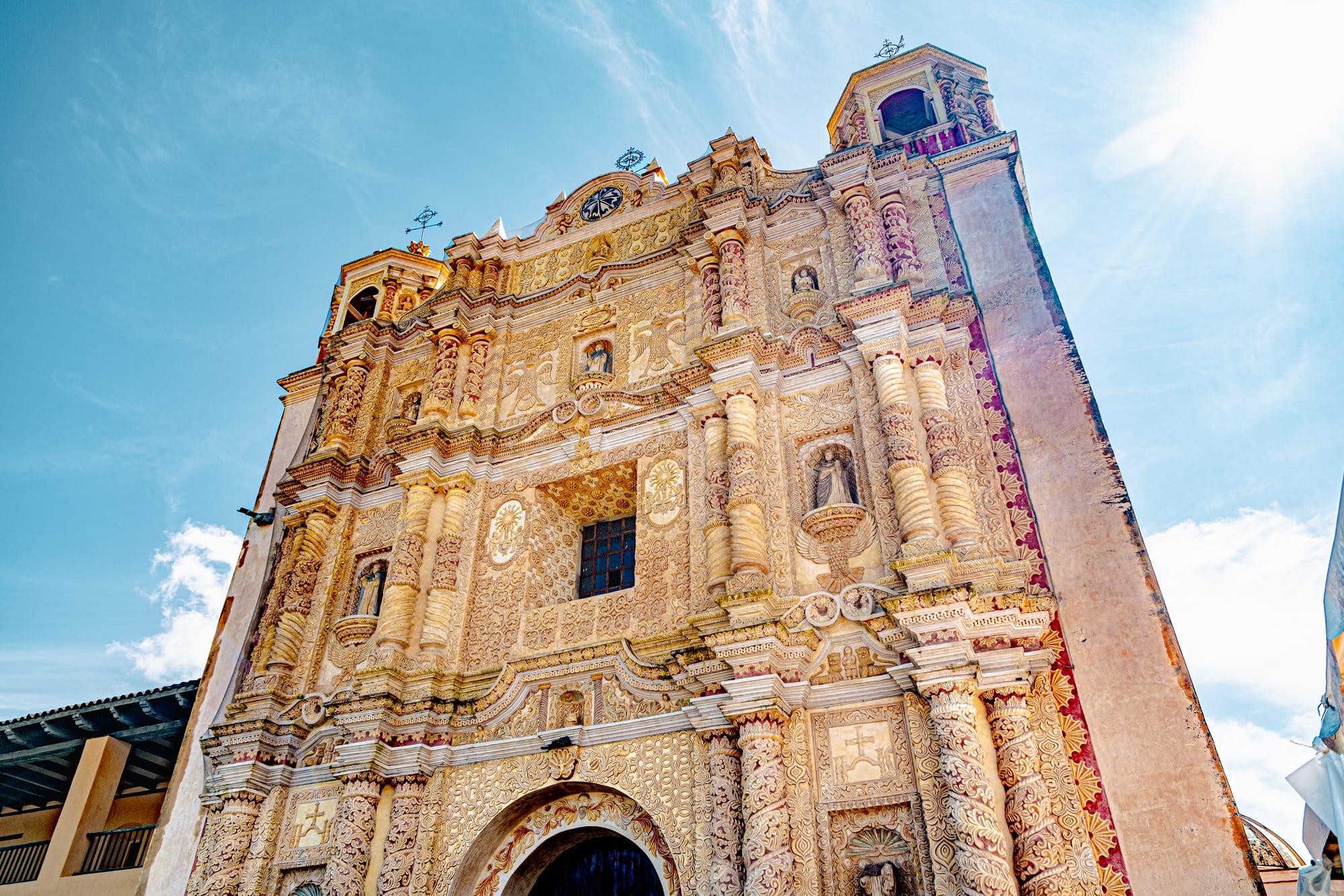 Ornate Baroque façade of Templo de Santo Domingo de Guzmán in San Cristóbal de las Casas, Chiapas, Mexico, featuring intricate stucco carvings, twisted columns, religious figures, and twin bell towers