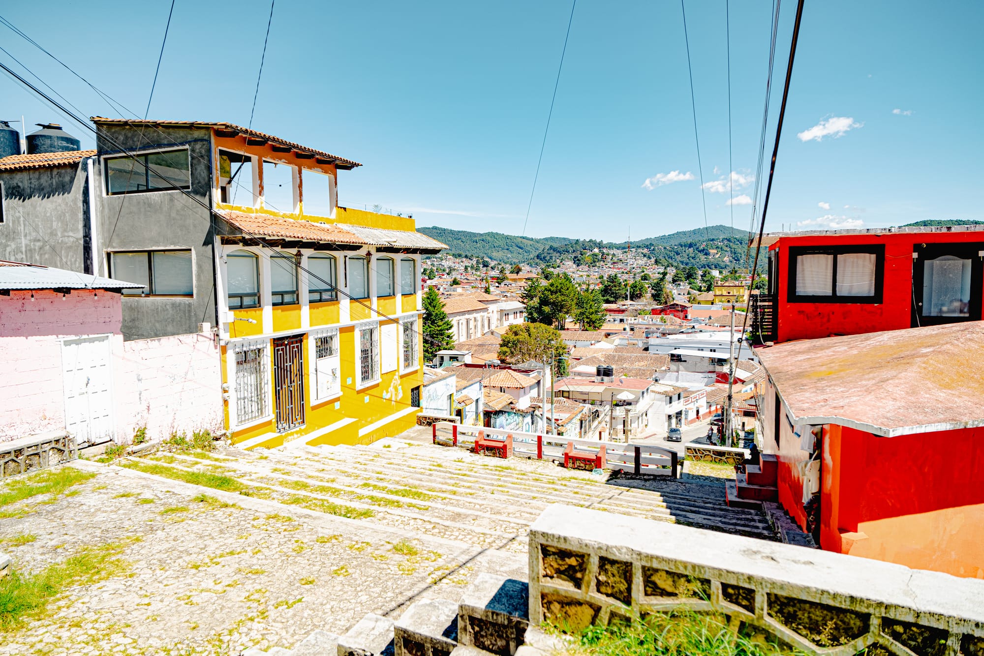 View over San Cristóbal de las Casas from the hillside staircase to Iglesia de San Cristóbalito, showing colorful neighborhood homes, stone steps, and the city spread across the valley in Chiapas, Mexico