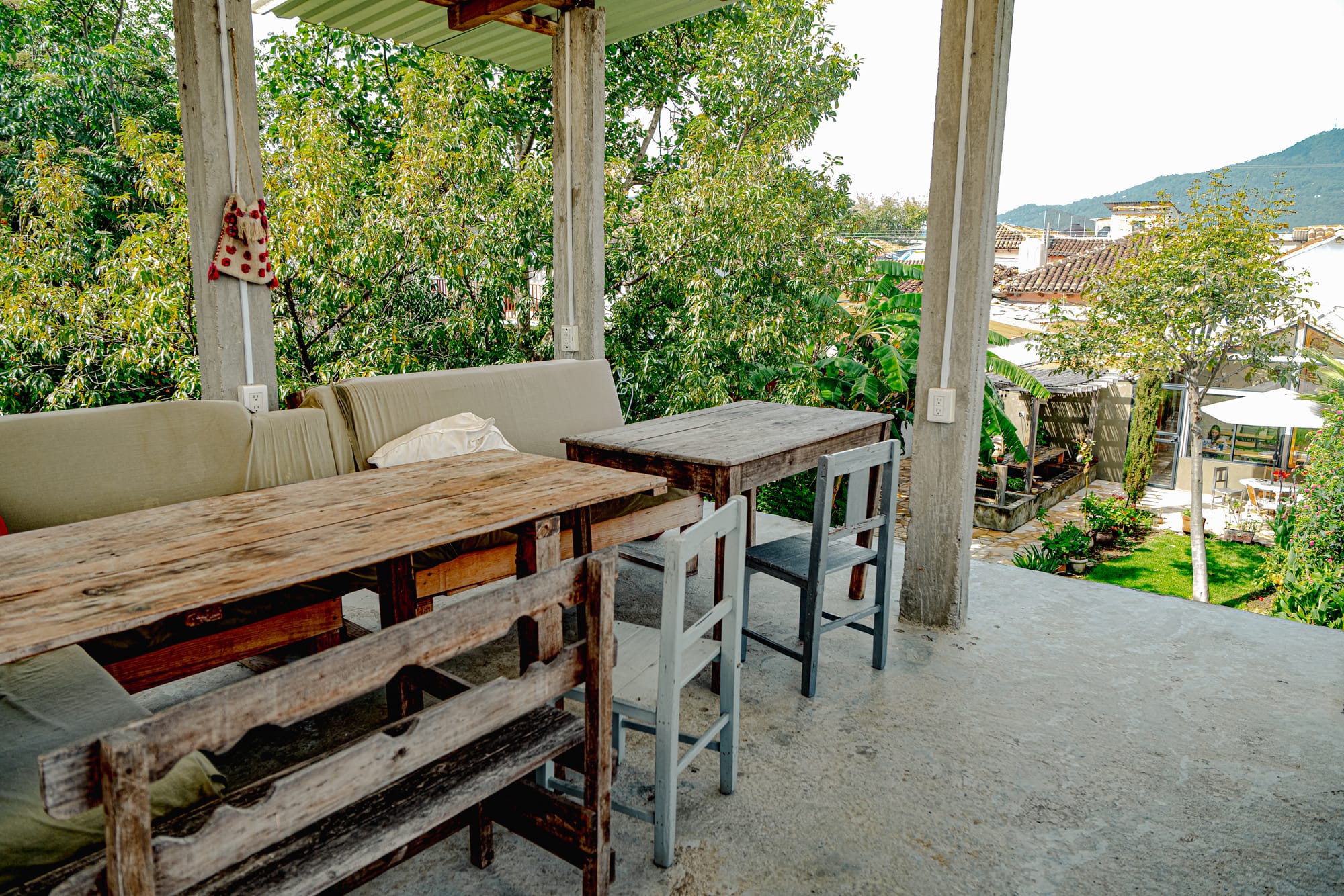 Rooftop terrace at Co404 coliving in San Cristóbal de las Casas, featuring rustic wooden tables, seating, and views overlooking the garden and surrounding greenery