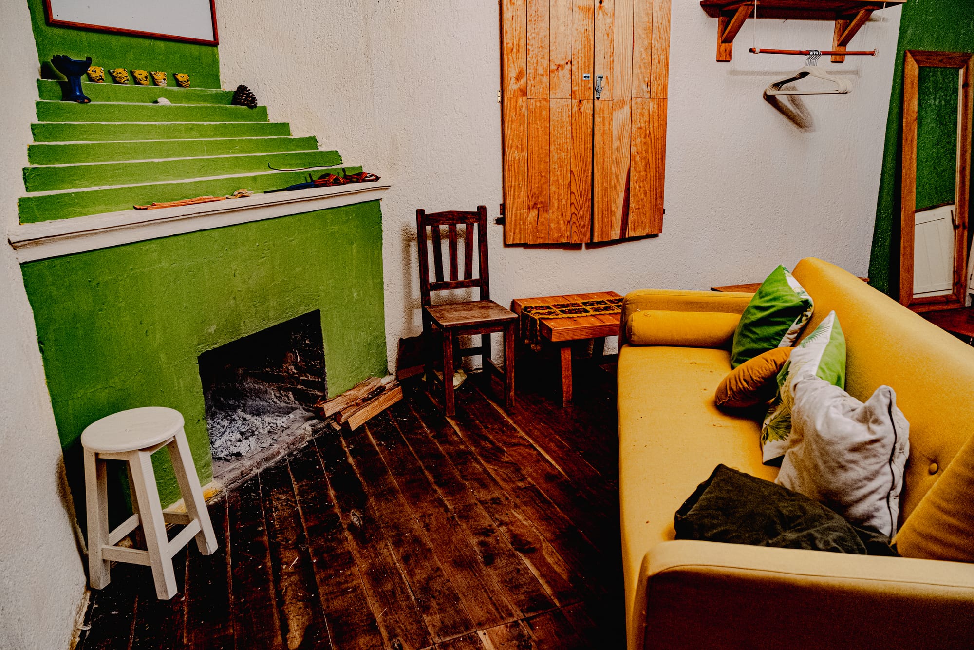 Cozy common room at Co404 coliving in San Cristóbal de las Casas, featuring a green fireplace, wooden furniture, and a yellow couch with pillows