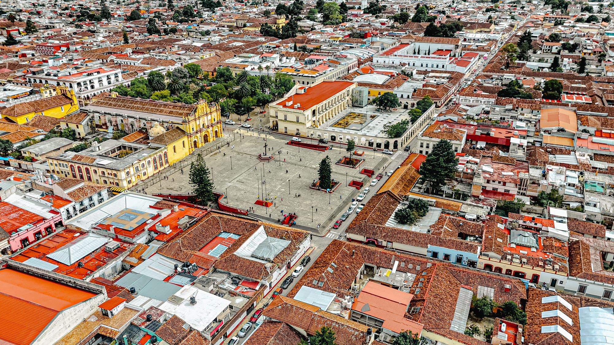 Drone view of the Cathedral of San Cristóbal de las Casas and the main plaza, surrounded by colonial buildings and red-tiled rooftops in the historic center