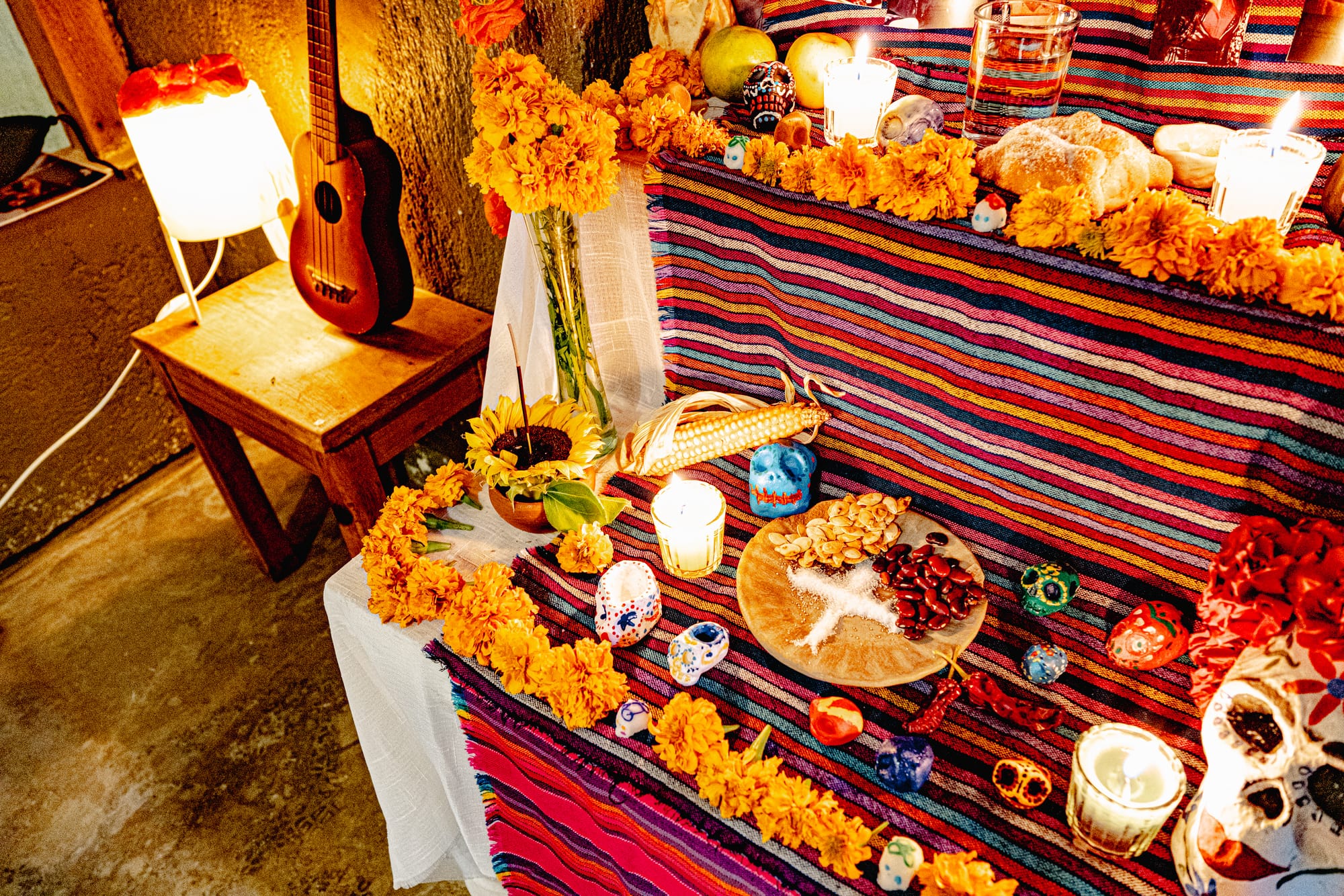 Day of the Dead altar in San Cristóbal de las Casas, Chiapas, Mexico, traditional Día de Muertos ofrenda with marigold flowers, candles, sugar skulls, pan de muerto, fruit, beans, corn, incense, and colorful woven textiles inside a local home