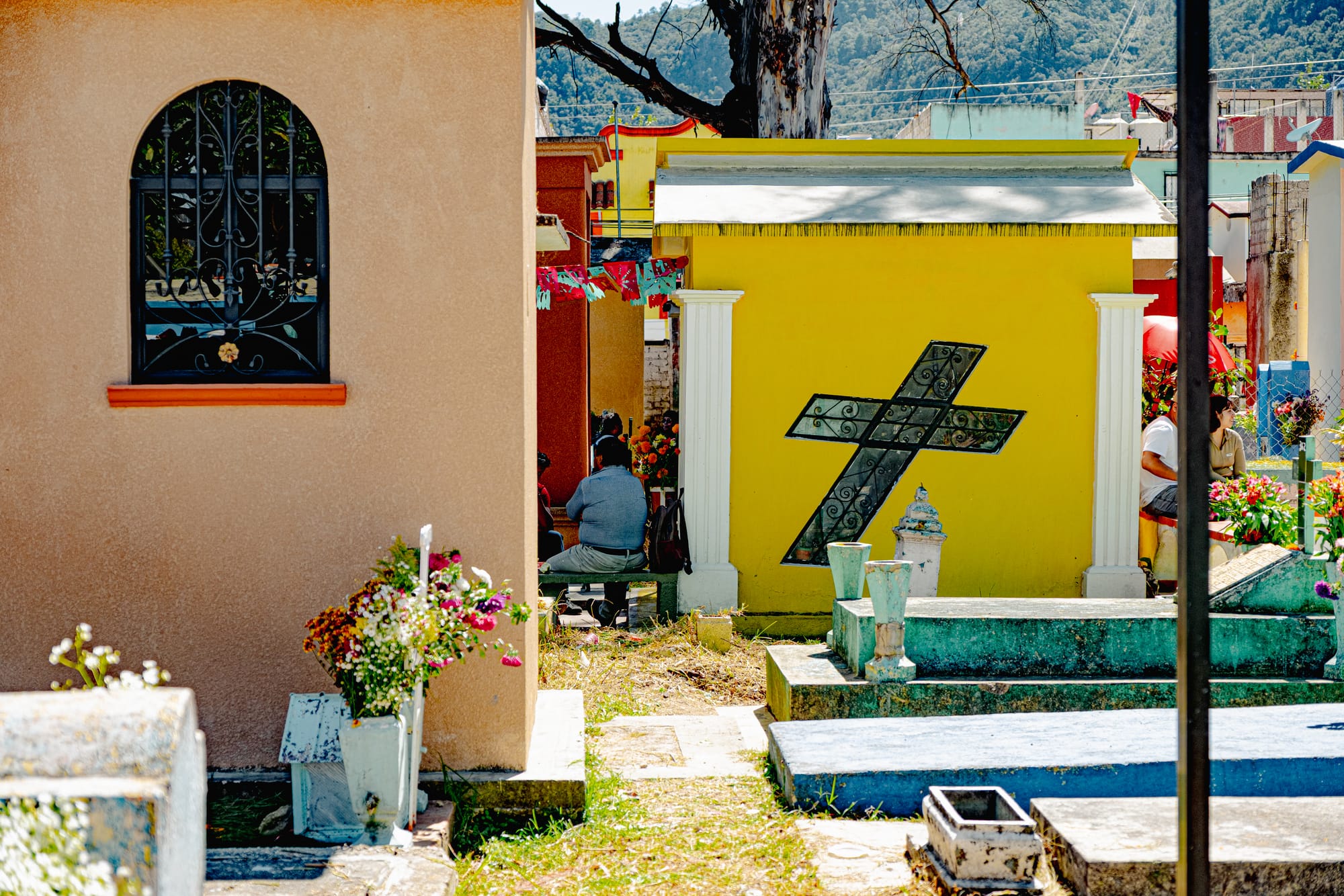 Día de Muertos at San Cristóbal Municipal Pantheon in San Cristóbal de las Casas, Chiapas, Mexico, colorful above ground tombs painted like small houses, yellow and pastel mausoleums with crosses, flowers placed beside graves, city cemetery architecture resembling a neighborhood during Day of the Dead