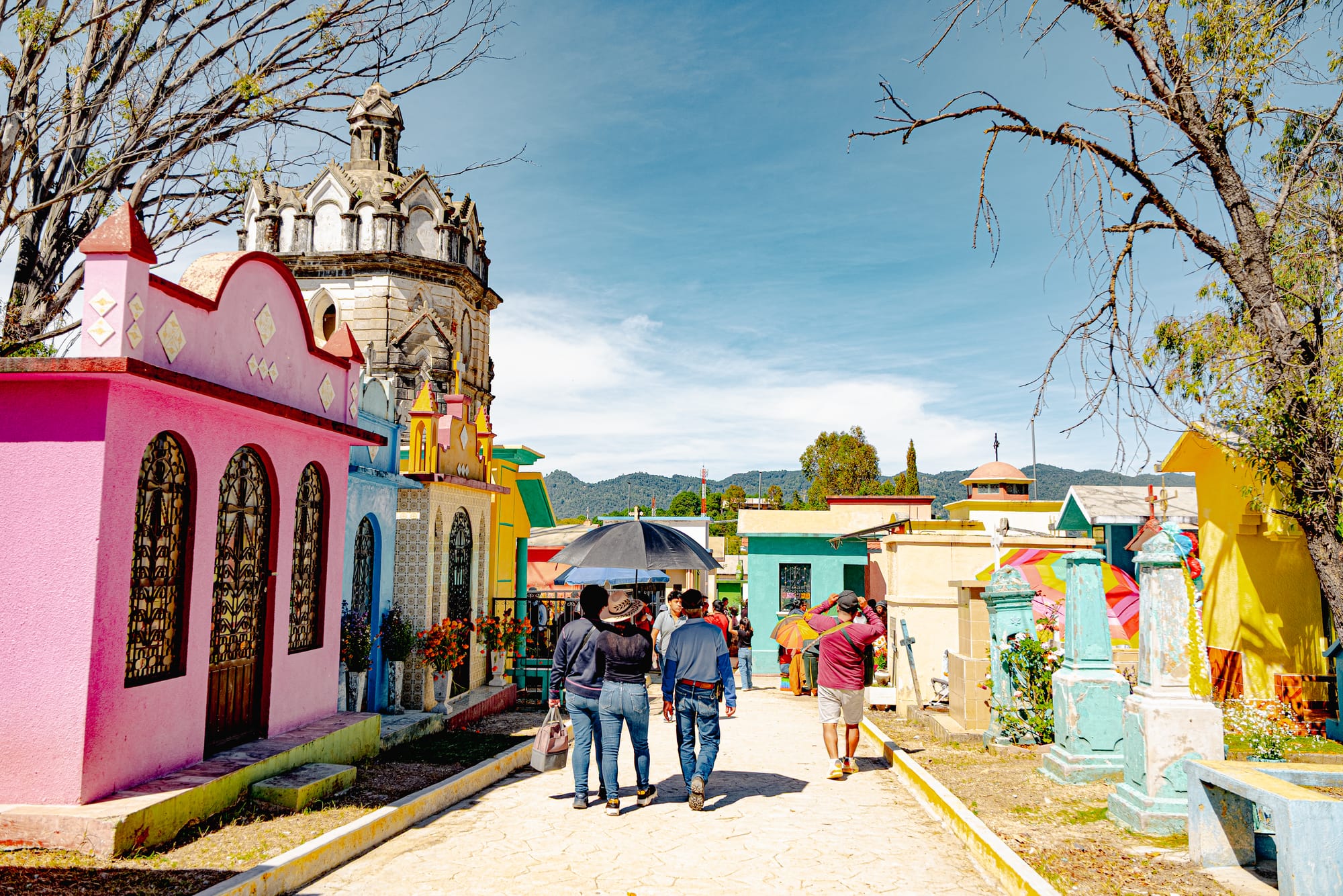 Día de Muertos at San Cristóbal Municipal Pantheon in San Cristóbal de las Casas, Chiapas, Mexico, colorful above ground tombs painted like small houses, people walking through cemetery streets with flowers, city cemetery resembling a small town during Day of the Dead celebrations with mountain backdrop