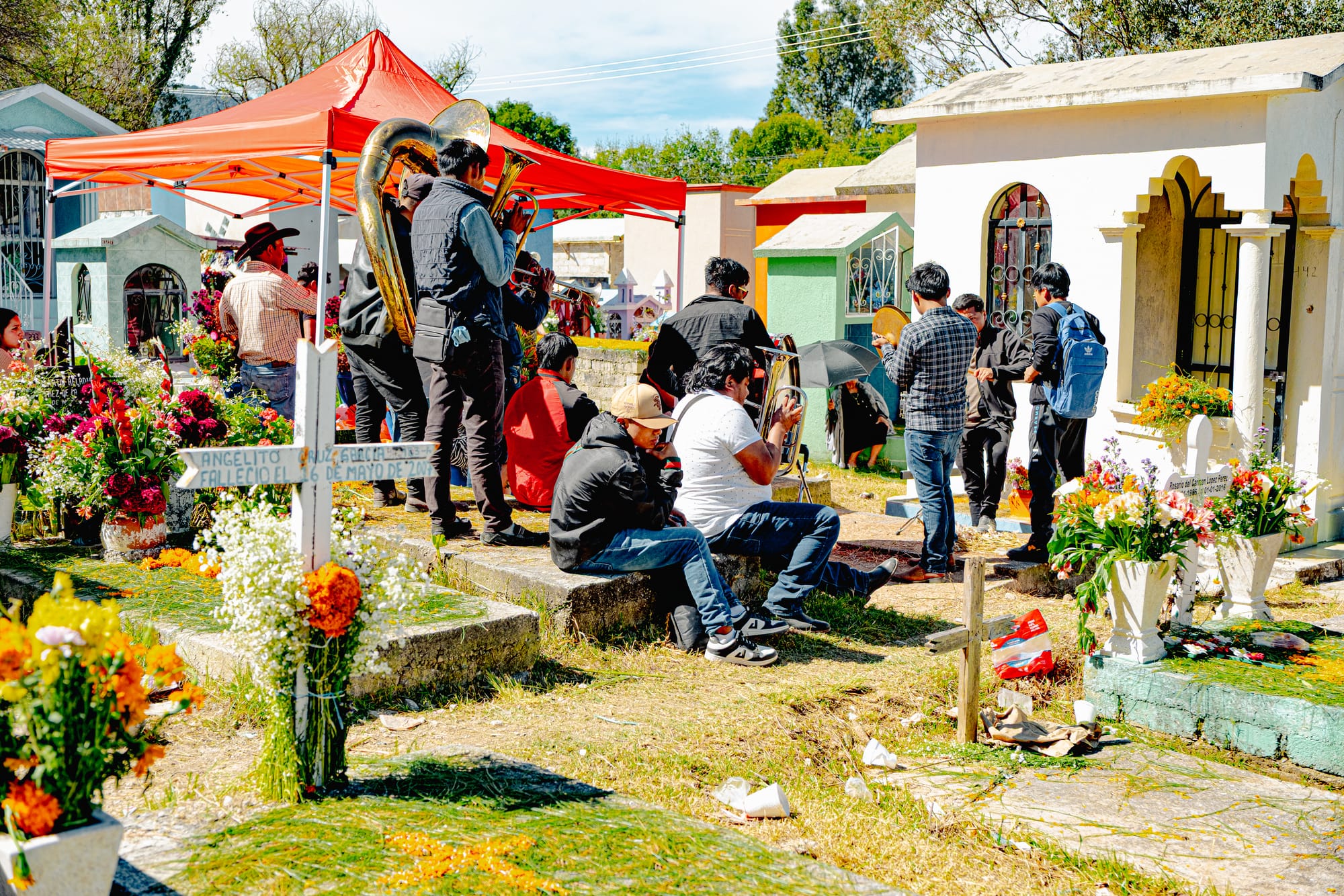 Día de Muertos at San Cristóbal Municipal Pantheon in San Cristóbal de las Casas, Chiapas, Mexico, brass band playing music among above ground tombs, local musicians performing beside colorful mausoleums, families gathered around graves with marigolds and flower arrangements during Day of the Dead cemetery celebrations
