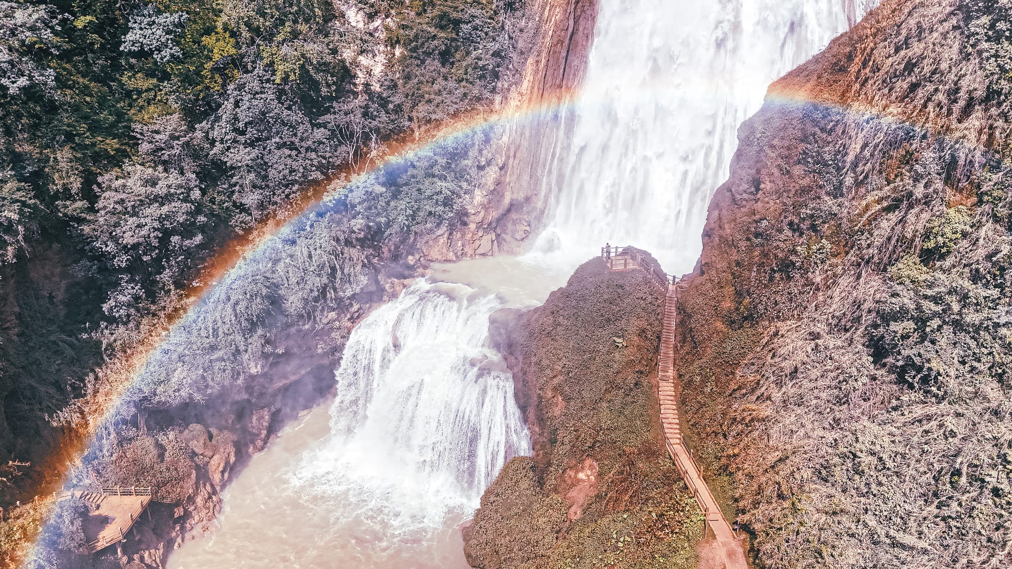 Velo de Novia waterfall at El Chiflón near San Cristóbal de Las Casas, Chiapas, Mexico, showing the upper and lower cascades with viewing platforms, stairway trail, mist, and a visible rainbow over the El Chiflón waterfalls park, a popular day trip often combined with Montebello Lakes