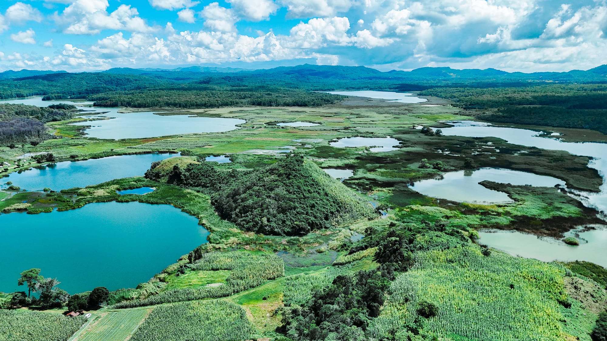 Aerial view of Montebello Lakes near San Cristóbal de Las Casas, Chiapas, Mexico, showing multiple interconnected lakes with varying shades of blue and green surrounded by forest, wetlands, and rolling hills, part of Lagunas de Montebello National Park often visited on a day trip combined with El Chiflón waterfalls