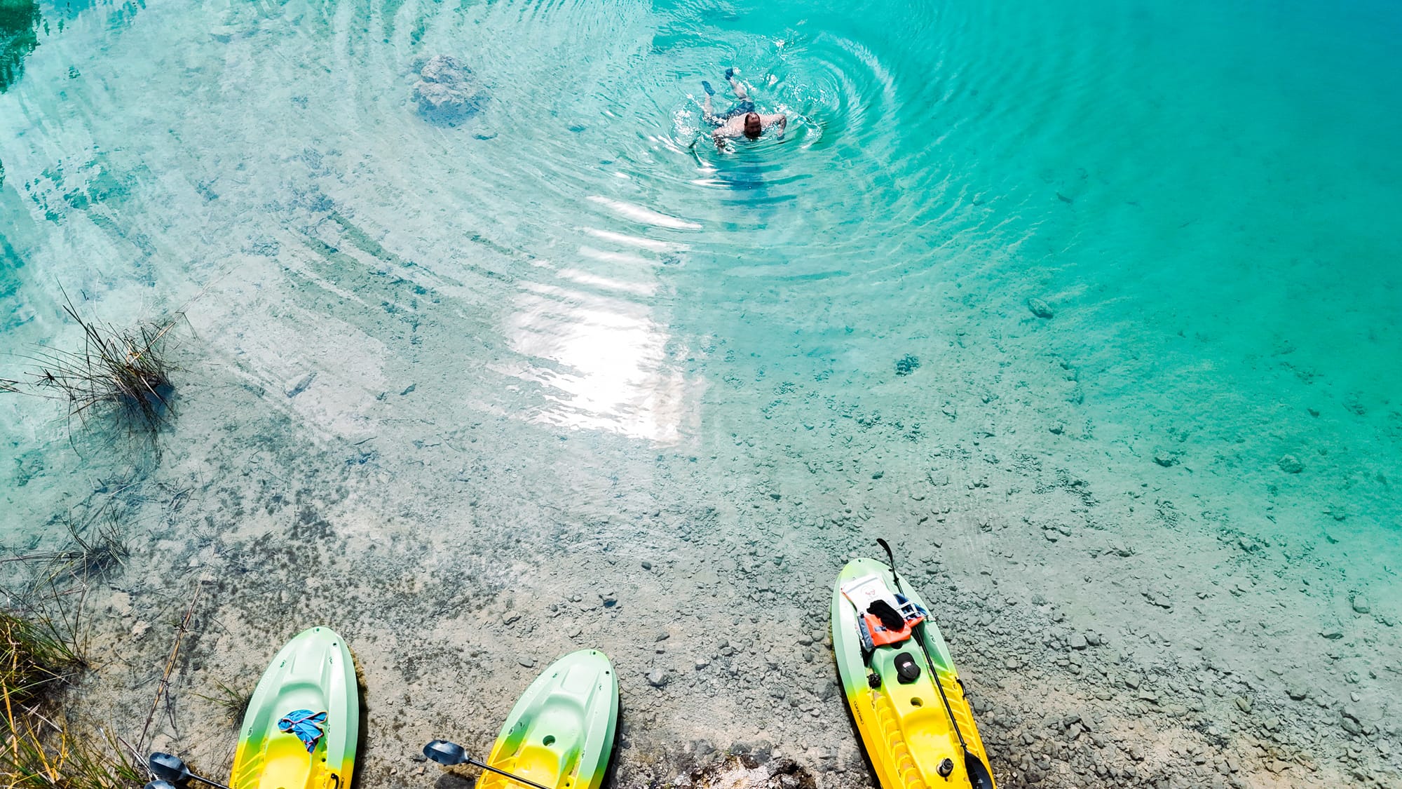 Clear turquoise lake at Montebello Lakes near San Cristóbal de Las Casas, Chiapas, Mexico, showing a person swimming in shallow transparent water with kayaks pulled up along the shoreline inside Lagunas de Montebello National Park, a popular stop on day trips often combined with El Chiflón waterfalls