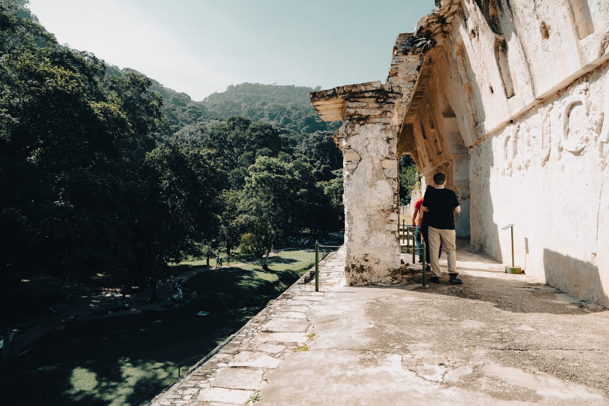 Palenque Palace corridor and exterior gallery overlooking jungle in Chiapas Mexico, visitors walking along ancient Maya stone walkway at Palenque archaeological site, elevated palace passage with carved walls and forested landscape below, exploring Palenque Mayan ruins near San Cristóbal de las Casas
