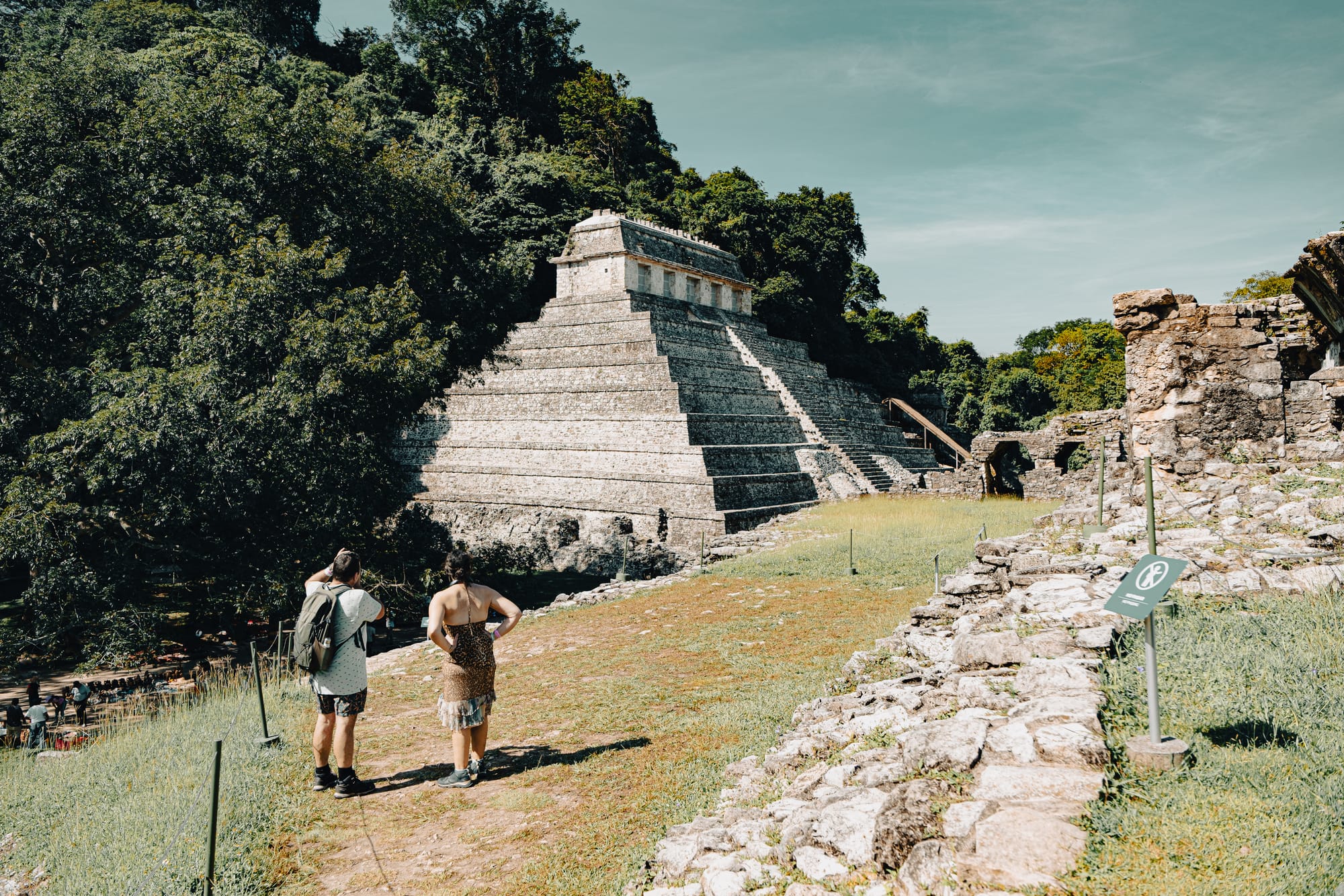 Palenque Mayan ruins Temple of the Inscriptions viewed from hillside path, visitors standing near stepped pyramid at Palenque archaeological site in Chiapas Mexico, iconic Maya temple surrounded by jungle landscape, people exploring ancient Mayan ruins near San Cristóbal de las Casas