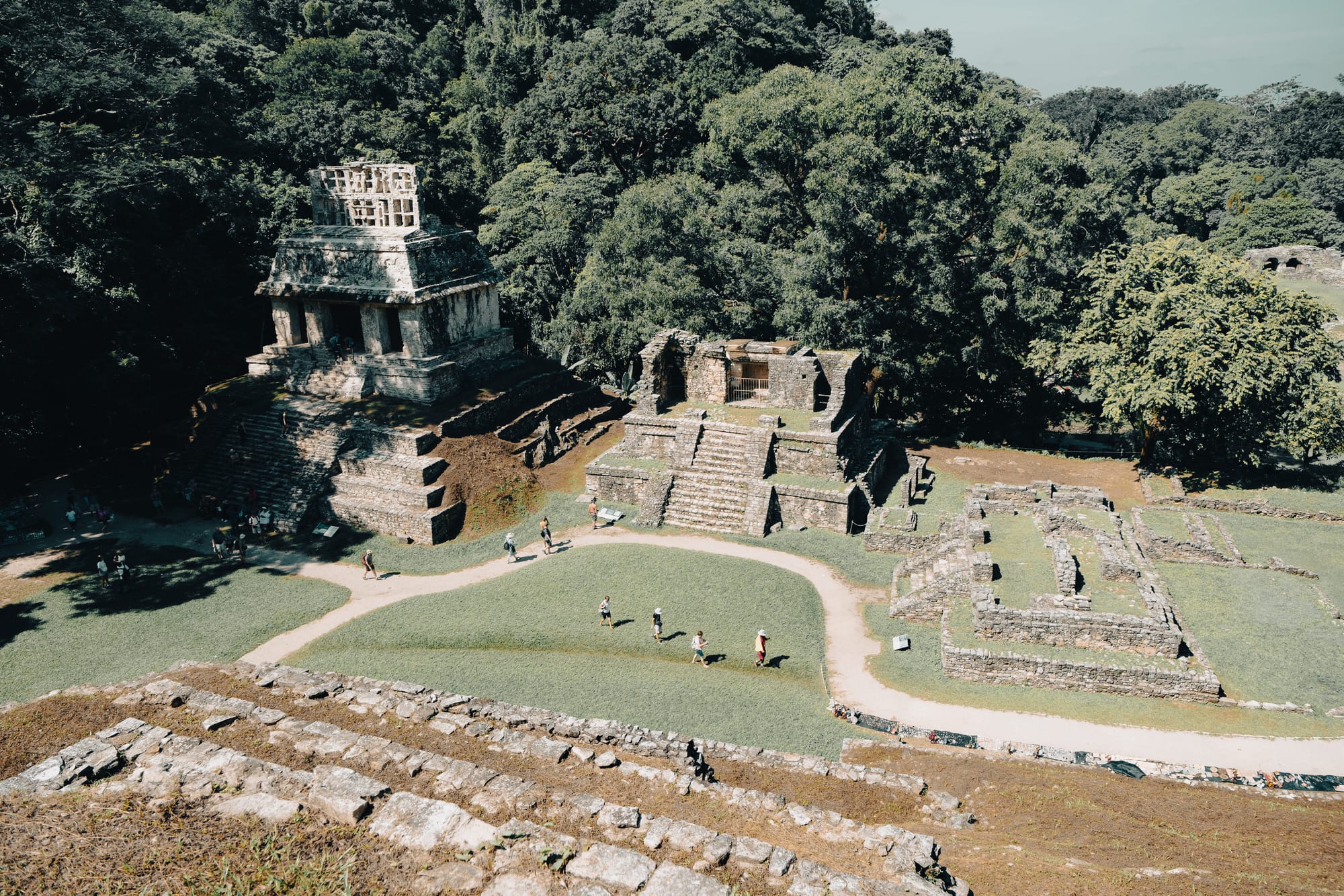Palenque Mayan ruins aerial perspective showing multiple temple structures and plazas surrounded by dense jungle in Chiapas Mexico, elevated view across Palenque archaeological site with ancient Maya buildings and pathways, iconic jungle ruins near San Cristóbal de las Casas with visitors walking between temples