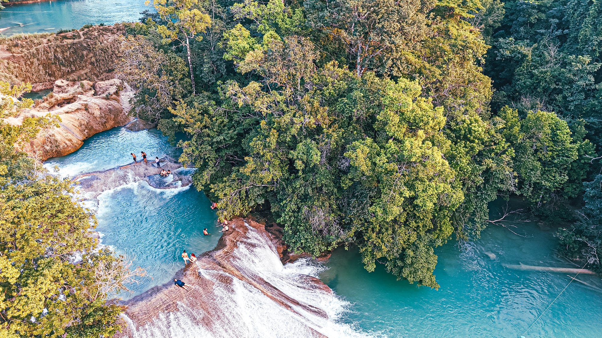 Cascadas Roberto Barrios waterfalls near Palenque, Chiapas, Mexico, aerial view of stepped limestone cascades and turquoise pools, people swimming and walking between waterfalls, dense jungle surroundings, Roberto Barrios waterfalls day trip near Palenque