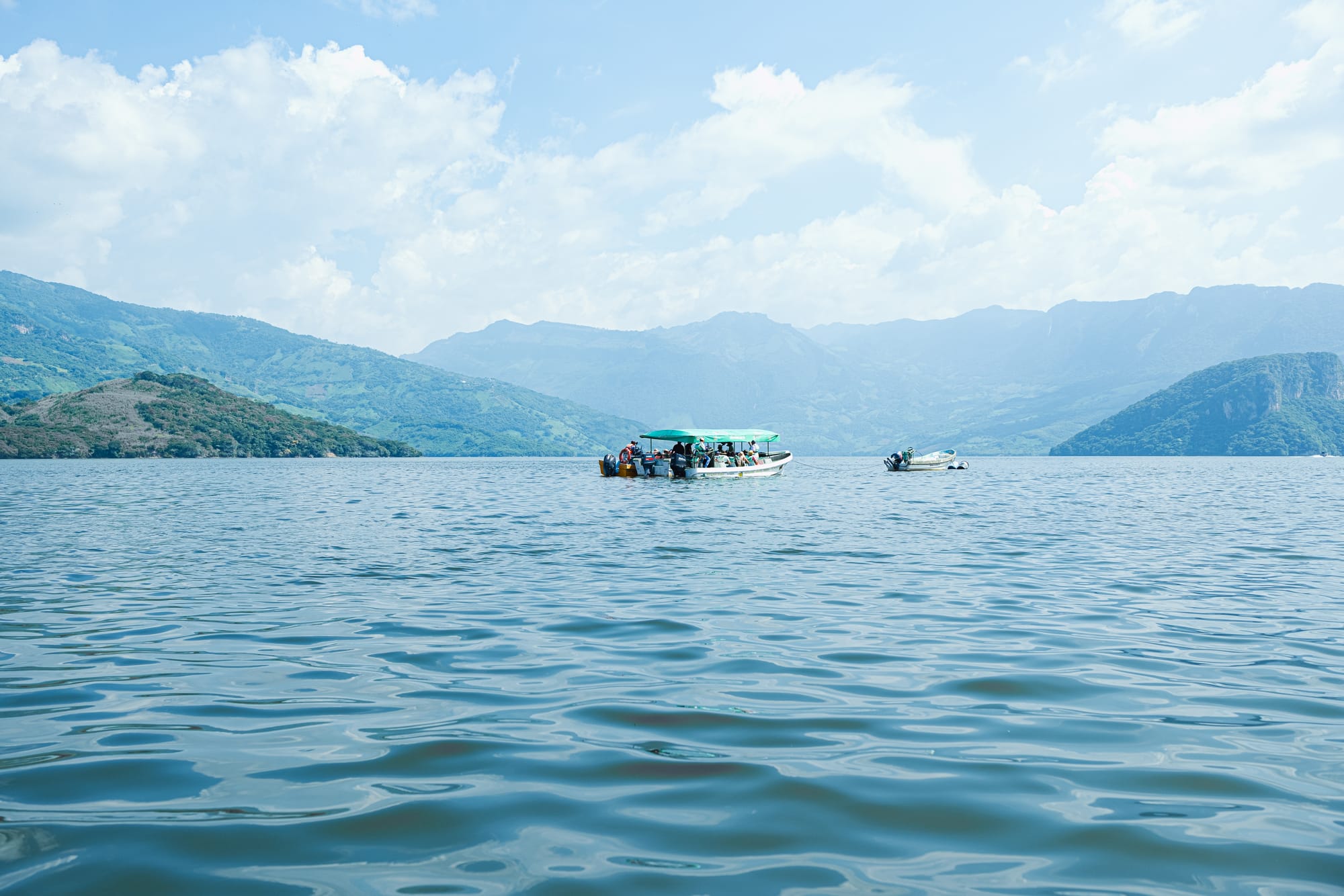 Tour boats on the wide Grijalva River near the entrance to Sumidero Canyon, with the green hills of Chiapas rising in the background under a bright sky