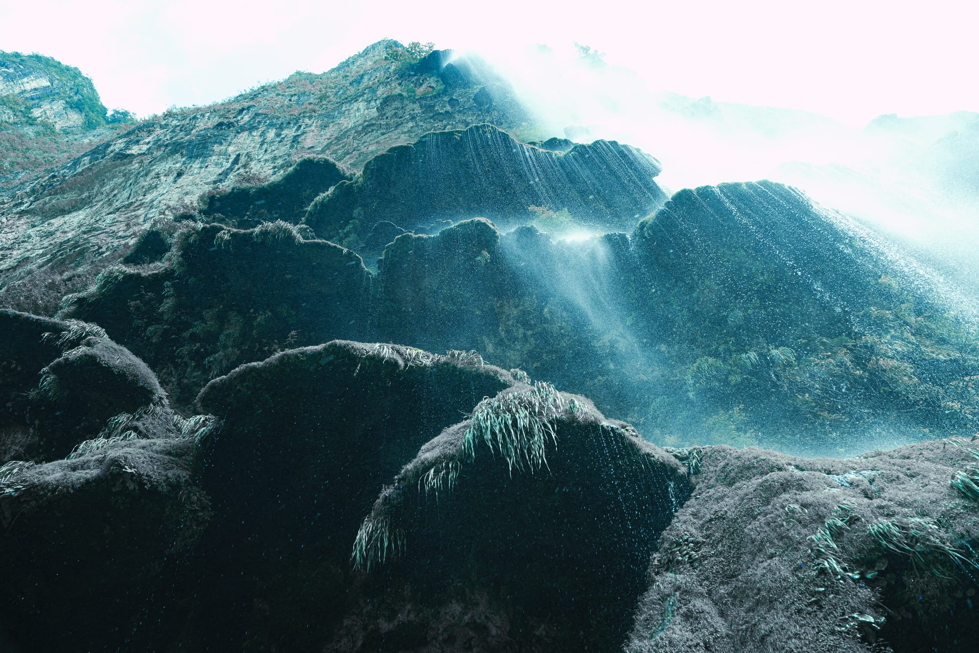 Looking up at the moss-covered “mushroom” waterfall in Sumidero Canyon, where mineral terraces catch the sunlight and water streams down the dark, rounded formations