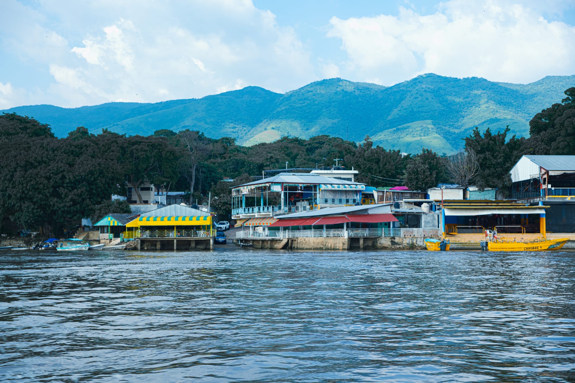 Waterfront buildings and restaurants in Chiapa de Corzo, seen from the river at the end of the Sumidero Canyon boat tour, with green hills rising in the background