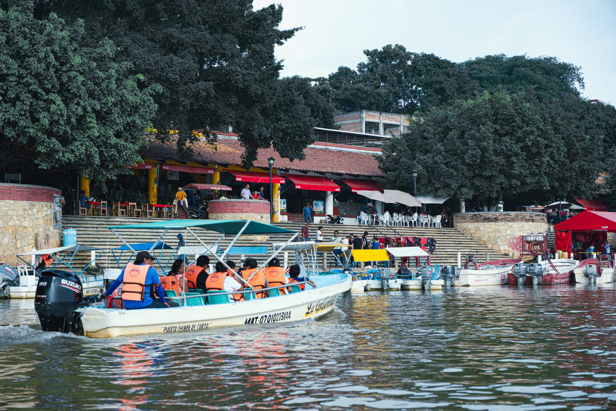 Tour boats pulling into the riverside dock at Chiapa de Corzo after a Sumidero Canyon boat tour, with restaurants and shaded terraces along the waterfront
