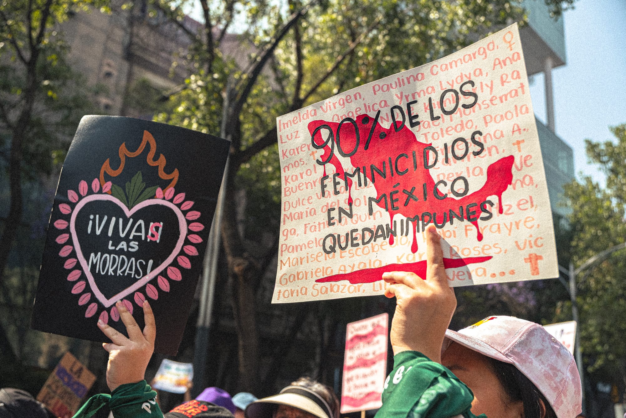 Feminist protest signs reading “90% de los feminicidios en México quedan impunes” and “Vivas las morras” during the 8M march in Mexico City