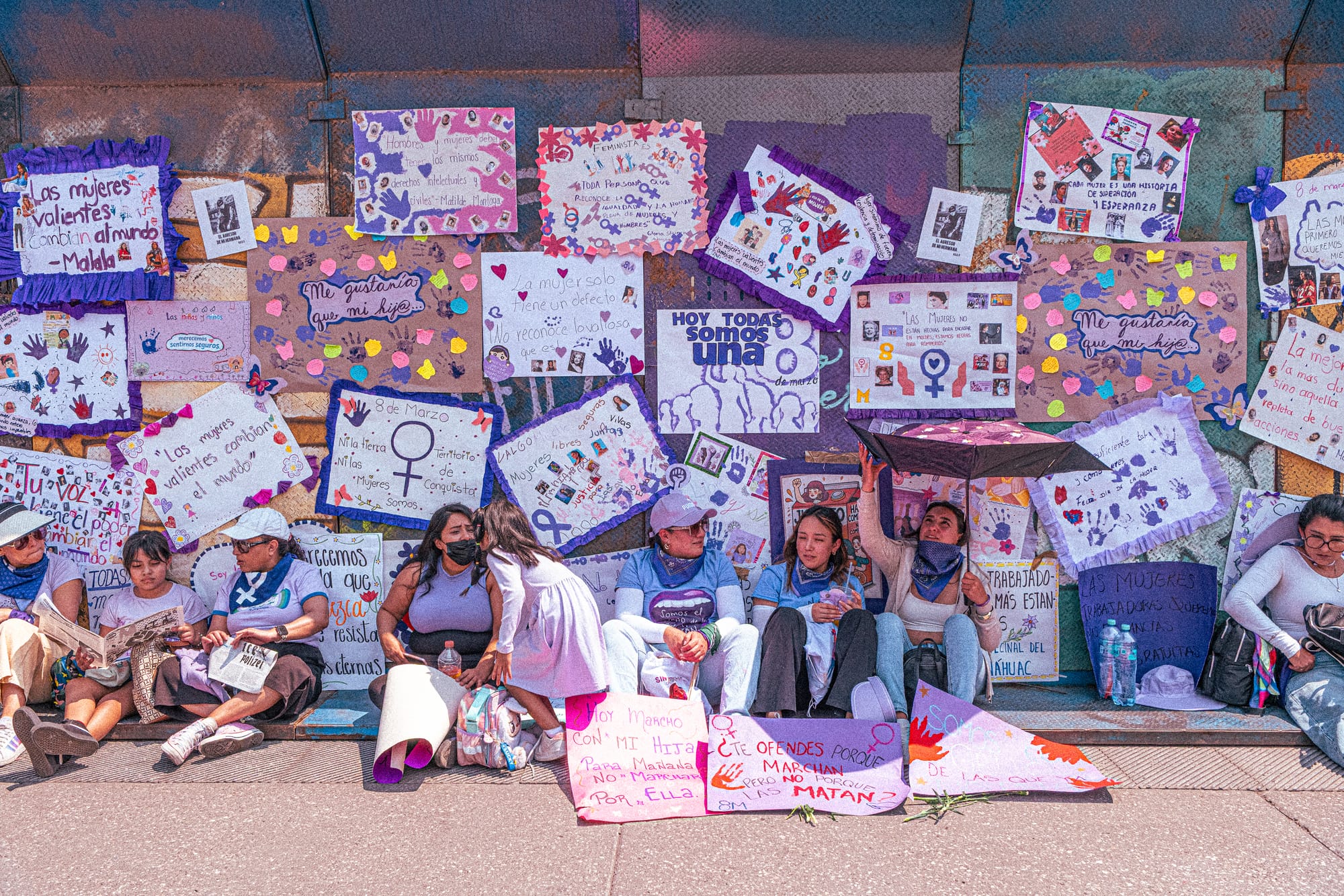 Mujeres descansando frente a un mural de carteles feministas durante la marcha 8M en Ciudad de México contra el feminicidio