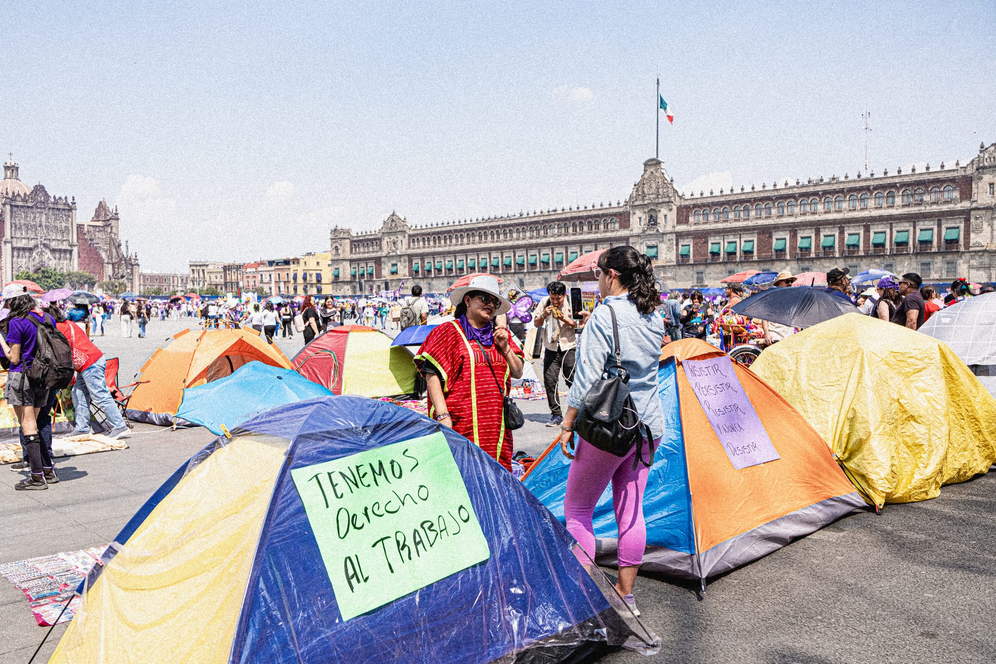 Women gathering around tents in the Zócalo during the 8M march in Mexico City with signs demanding labor rights and gender equality