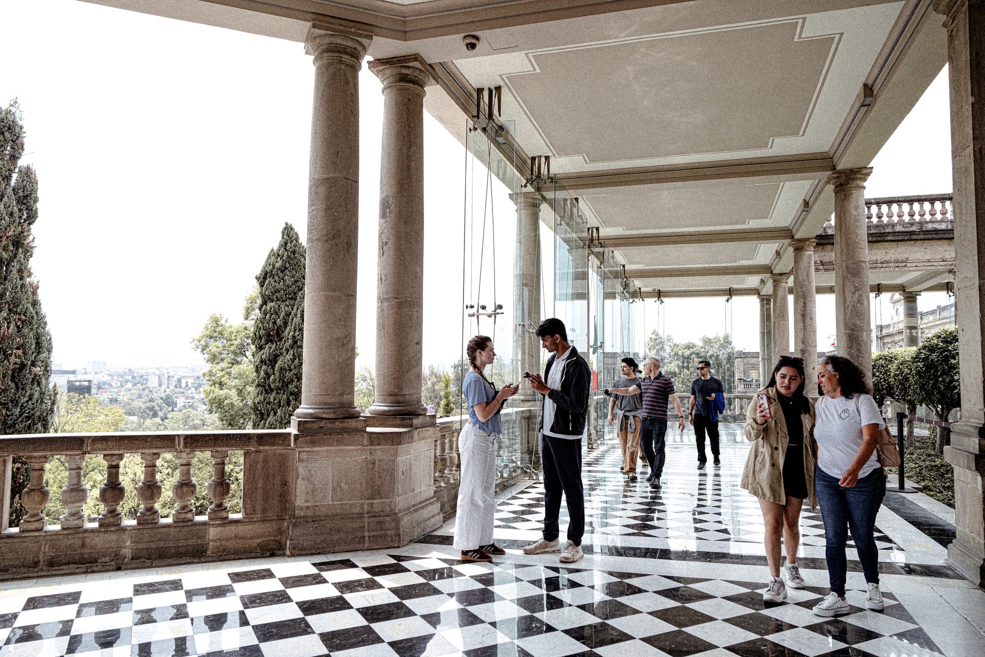 Visitors walking through Chapultepec Castle Mexico City terrace corridor with checkered floors and views over Chapultepec Park