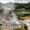 Steam rises from a bubbling geothermal pool surrounded by greenery and hills