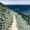 A narrow dirt trail curves along a steep coastal hillside, appearing to lead directly into the vast blue Atlantic Ocean under an open sky