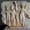 Stone relief of four figures in partial profile, three nude or semi-nude with arms linked, led by a larger central figure wearing a radiant crown and robe, possibly representing a deity