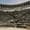 Visitors sit scattered across the steep, curved stone seating of the ancient Aspendos amphitheater under a hazy sky