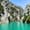 A tour boat glides through the vivid turquoise waters of Green Canyon, surrounded by steep, pine-covered limestone cliffs under a clear blue sky