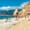 Swimmers and sunbathers on the pebbled beach of Suluada, backed by jagged cliffs and turquoise Mediterranean water