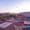 View from the rooftop of Nomad Cave Hotel in Cappadocia at sunrise: patterned rugs and cushions spread across the terrace, with dozens of hot air balloons floating above