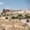 ATV riders drive along a dusty trail in Cappadocia with a backdrop of ancient cave dwellings and rock formations under a bright blue sky
