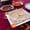 A square white plate of hummus drizzled with olive oil and garnished with carrot slices, served on a red patterned tablecloth with side dishes